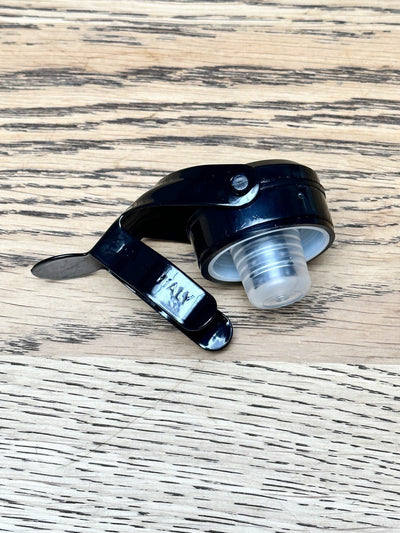Black champagne stopper with a clear silicone seal and a lever mechanism, resting on a wooden surface.